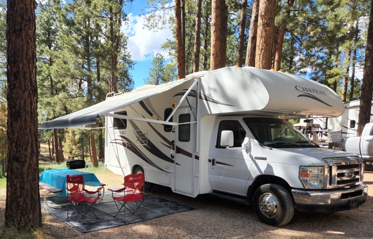 High-quality RV with large automatic awning, equipped with outdoor living space that has 4 camp chairs, outdoor rug, table, and grill.