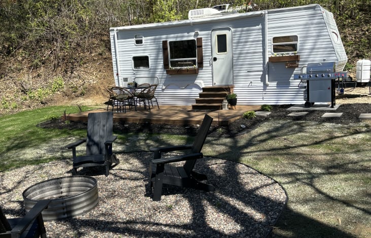 Exterior of camper includes outdoor seating area on the patio and around the fire pit, gas grill, outdoor games, and more!