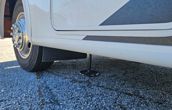 Close-up view of the left hydraulic leveling jack on the 2024 Thor ACE 32B motorhome, showcasing its sturdy construction and precise ground support for stable leveling.