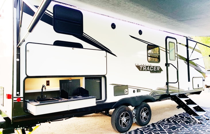 Outside of trailer with outside kitchen area that includes a sink, grill and mini fridge. The large outdoor rug is included.