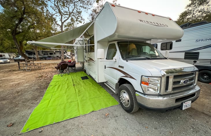 Equipped with awning, outdoor mat, 4 camping chairs, firepit, and BBQ grill.